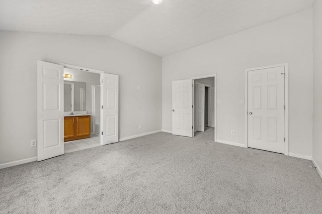 unfurnished bedroom featuring light colored carpet, connected bathroom, and vaulted ceiling