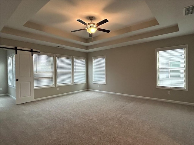 carpeted empty room featuring a tray ceiling, a barn door, and ceiling fan