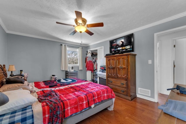 bedroom with baseboards, visible vents, wood finished floors, crown molding, and a textured ceiling