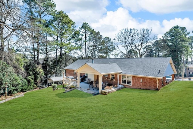 back of property featuring a yard, brick siding, a patio, and a shingled roof