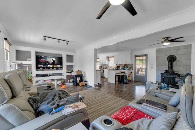 living room featuring ceiling fan, wood finished floors, a wood stove, and rail lighting