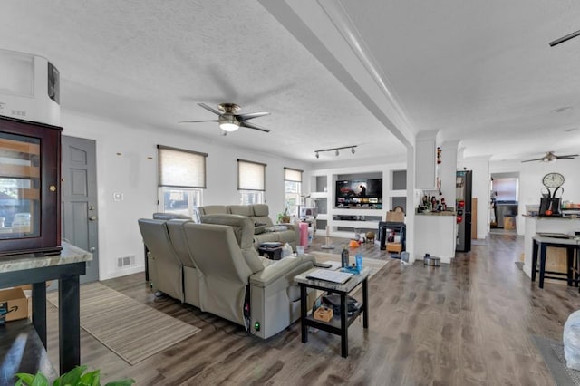 living area featuring a textured ceiling, a fireplace, wood finished floors, visible vents, and a ceiling fan