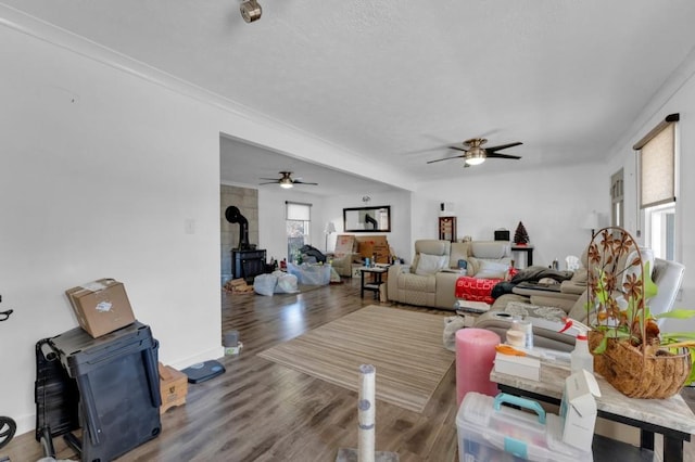 living area with a wood stove, ceiling fan, and wood finished floors