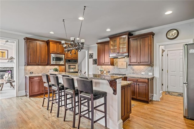 kitchen featuring under cabinet range hood, a notable chandelier, ornamental molding, a breakfast bar, and stainless steel appliances