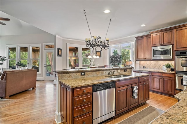 kitchen with a sink, stainless steel appliances, open floor plan, light wood-type flooring, and a center island with sink