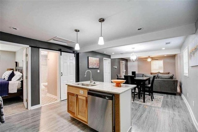 kitchen featuring stainless steel dishwasher, sink, a barn door, a center island with sink, and light hardwood / wood-style flooring