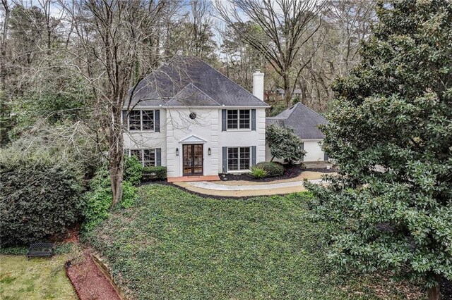 colonial home with french doors, a chimney, and a front lawn