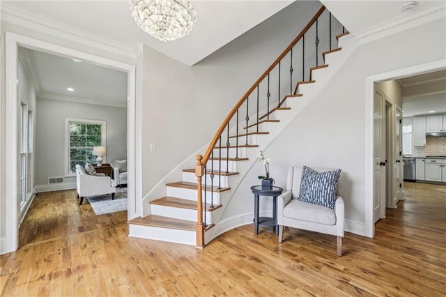 staircase featuring wood finished floors, baseboards, a chandelier, and ornamental molding