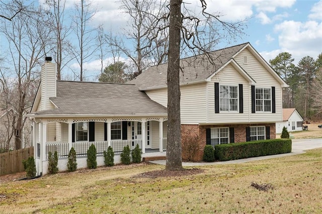 split level home with brick siding, a chimney, covered porch, fence, and a front lawn