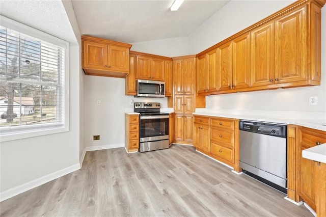 kitchen with brown cabinetry, light wood-style flooring, appliances with stainless steel finishes, and light countertops