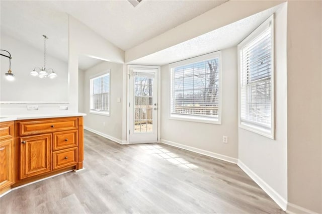 interior space featuring a chandelier, lofted ceiling, light wood-style flooring, and baseboards