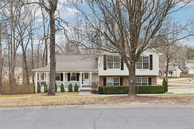 split level home featuring roof with shingles, fence, a porch, and brick siding