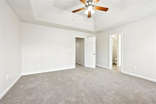 unfurnished bedroom featuring baseboards, a tray ceiling, carpet flooring, and ensuite bathroom