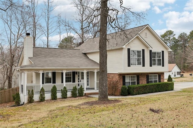 split level home with brick siding, a chimney, covered porch, a front yard, and fence