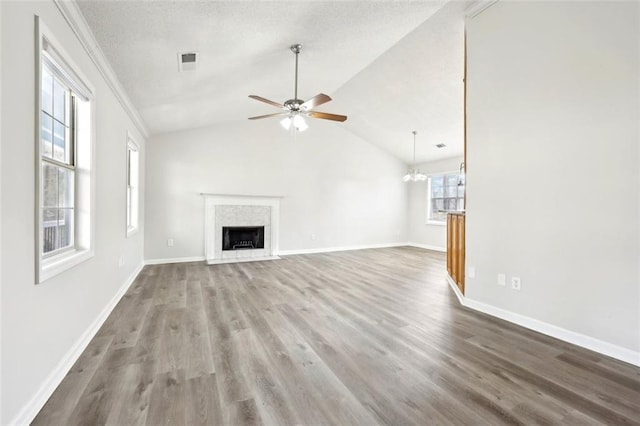 unfurnished living room with lofted ceiling, ceiling fan with notable chandelier, wood finished floors, a fireplace with flush hearth, and visible vents