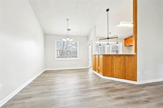 unfurnished dining area with a notable chandelier, plenty of natural light, a textured ceiling, and light wood finished floors