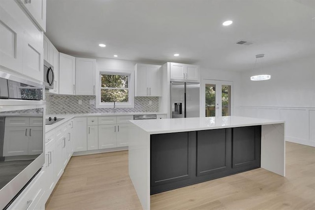 kitchen with white cabinets, appliances with stainless steel finishes, a center island, decorative backsplash, and hanging light fixtures