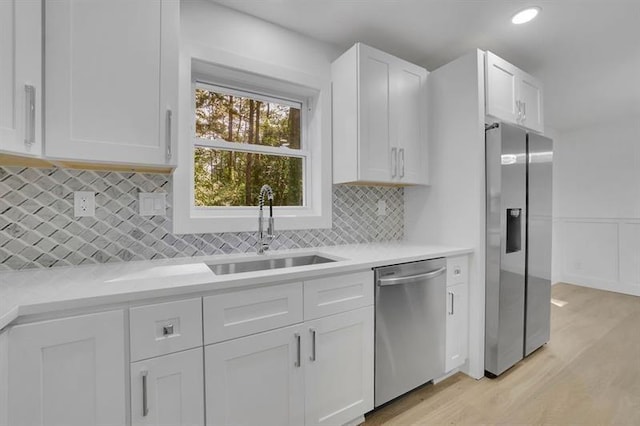 kitchen featuring white cabinetry, stainless steel appliances, decorative backsplash, light wood-type flooring, and sink