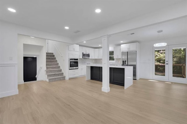 kitchen featuring decorative light fixtures, light hardwood / wood-style floors, decorative backsplash, white cabinetry, and appliances with stainless steel finishes