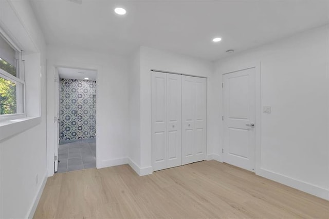 unfurnished bedroom featuring light wood-type flooring, ensuite bath, and a closet