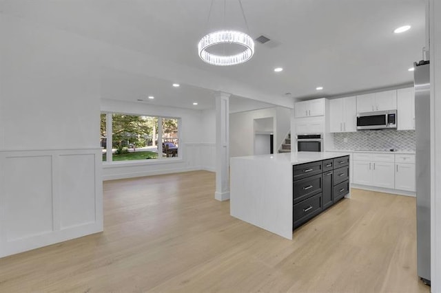 kitchen featuring white cabinetry, light hardwood / wood-style floors, stainless steel appliances, tasteful backsplash, and decorative light fixtures