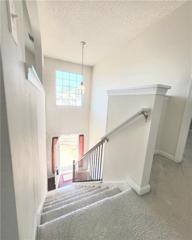 stairway featuring carpet floors, a towering ceiling, and a textured ceiling