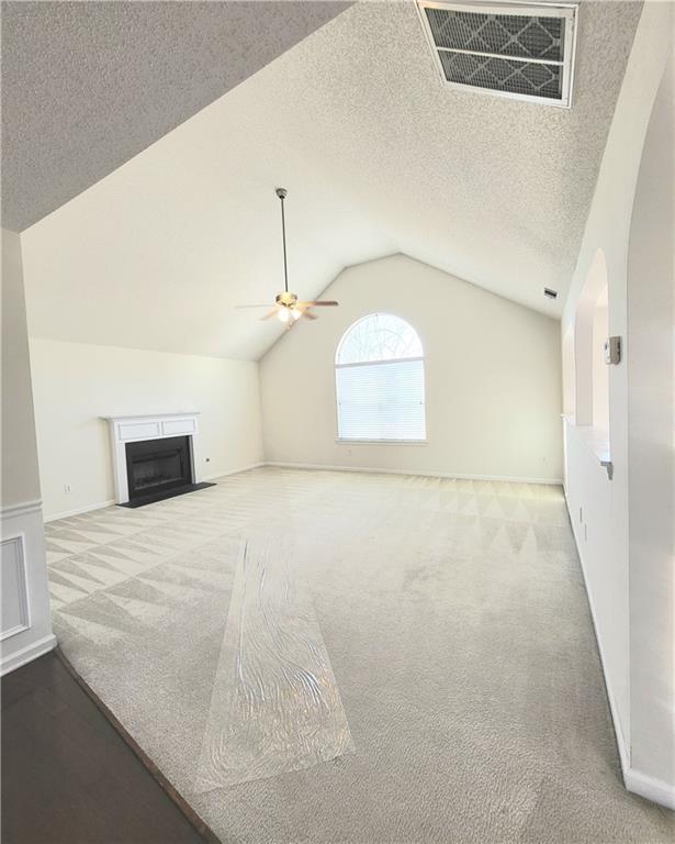 unfurnished living room featuring ceiling fan, light colored carpet, a textured ceiling, and lofted ceiling