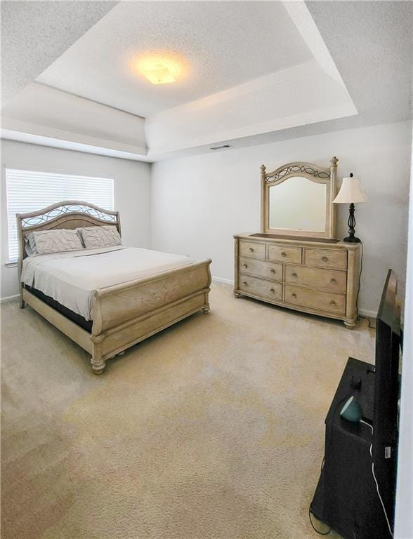 bedroom featuring light colored carpet, a tray ceiling, and a textured ceiling