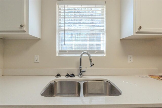 kitchen with light countertops, white cabinetry, and a sink