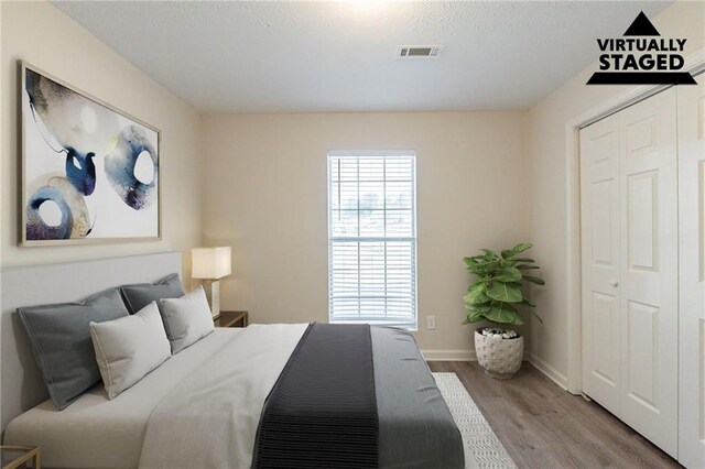 bedroom with a closet, wood finished floors, visible vents, and baseboards