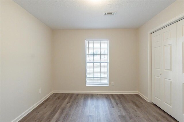 unfurnished bedroom featuring a closet, wood finished floors, visible vents, and baseboards