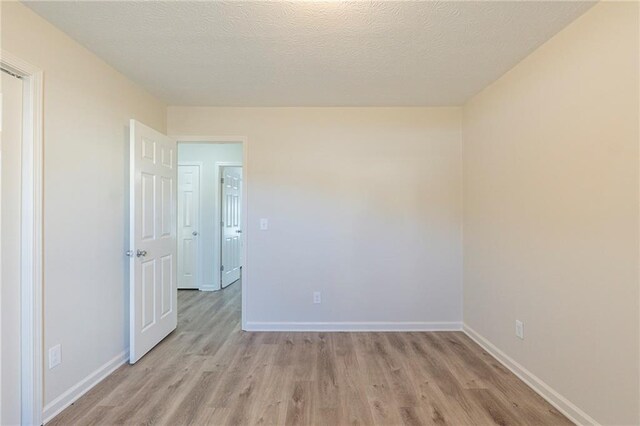 empty room featuring baseboards, a textured ceiling, and light wood-style floors