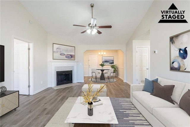 living area with a fireplace, vaulted ceiling, baseboards, and wood finished floors