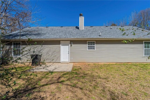 back of house featuring a yard, roof with shingles, a chimney, and a patio