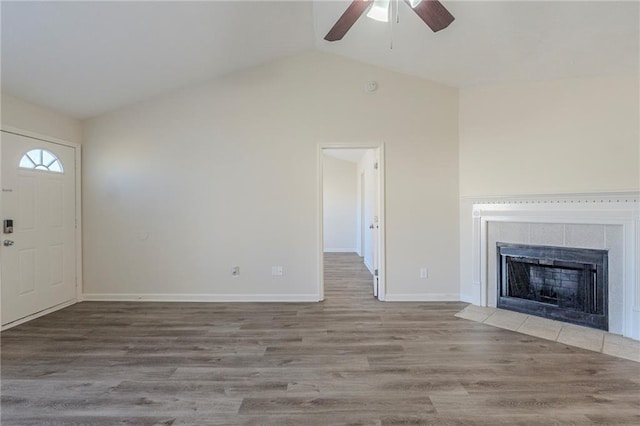 unfurnished living room with baseboards, a tile fireplace, lofted ceiling, ceiling fan, and wood finished floors