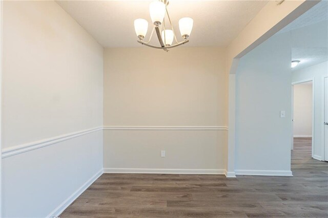 unfurnished dining area featuring a notable chandelier, baseboards, and wood finished floors