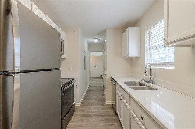 kitchen featuring stainless steel appliances, light countertops, light wood-type flooring, white cabinetry, and a sink