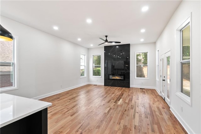 unfurnished living room featuring ceiling fan, light hardwood / wood-style floors, and a high end fireplace