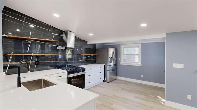 kitchen featuring wall chimney range hood, white cabinetry, sink, light hardwood / wood-style floors, and stainless steel appliances