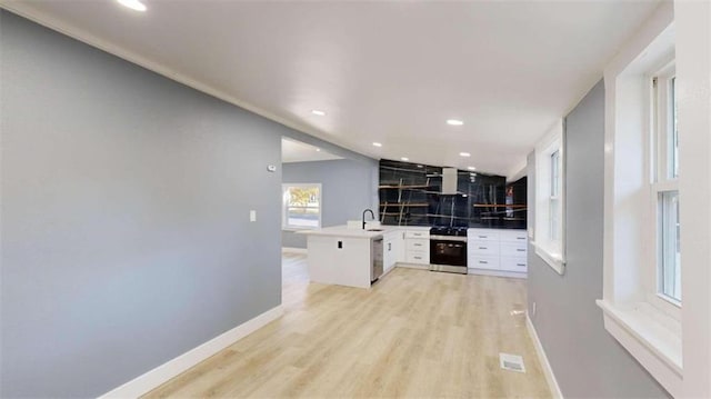 kitchen with kitchen peninsula, white cabinetry, light wood-type flooring, range hood, and stainless steel appliances