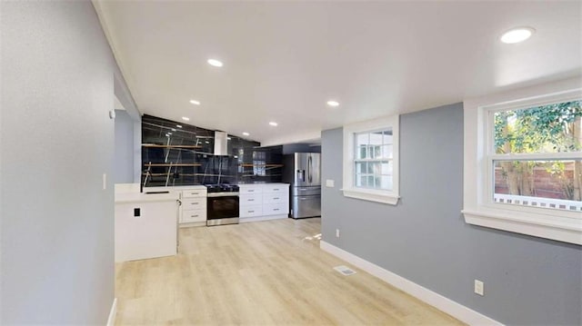 kitchen with extractor fan, appliances with stainless steel finishes, light wood-type flooring, and white cabinets