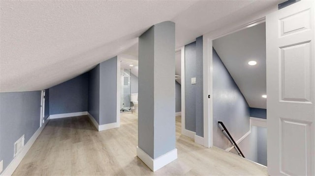 additional living space with vaulted ceiling, light hardwood / wood-style flooring, and a textured ceiling