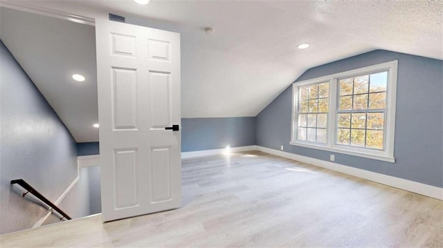 additional living space featuring light hardwood / wood-style floors, a textured ceiling, and vaulted ceiling