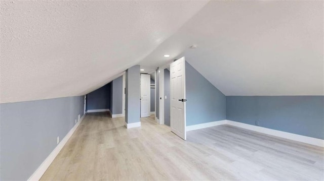 bonus room featuring vaulted ceiling, a textured ceiling, and light hardwood / wood-style floors