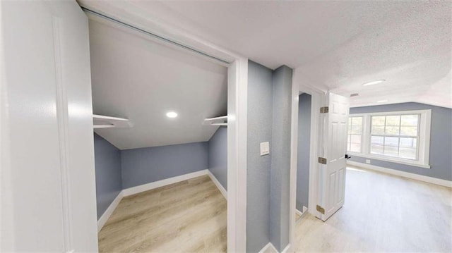 corridor featuring light hardwood / wood-style flooring, a textured ceiling, and lofted ceiling