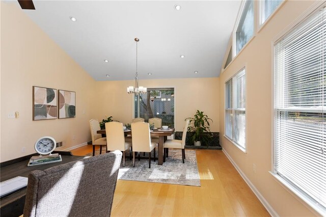 dining area with light hardwood / wood-style floors, high vaulted ceiling, and an inviting chandelier