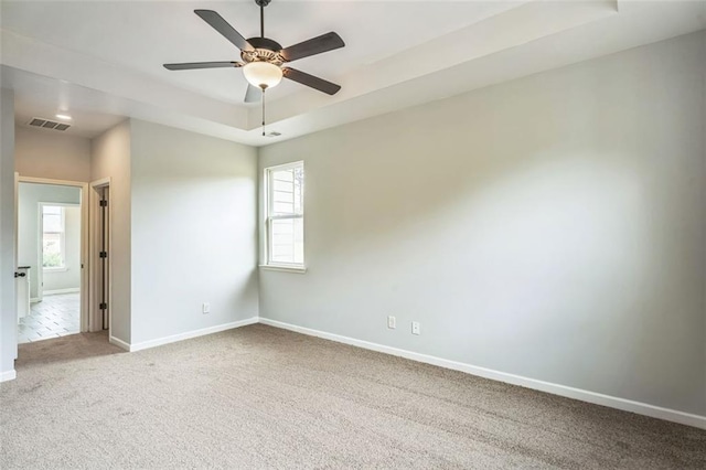 carpeted spare room featuring a tray ceiling, visible vents, ceiling fan, and baseboards