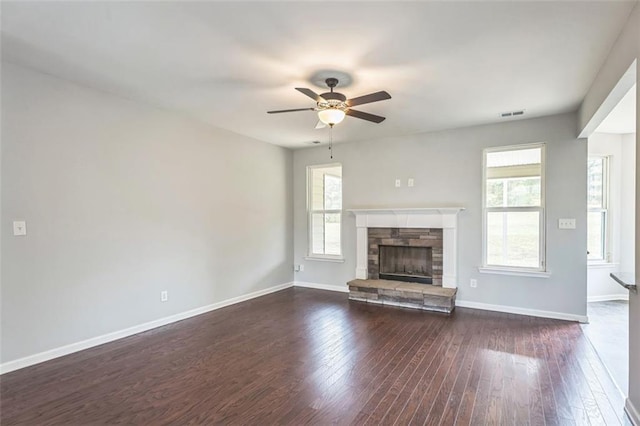 unfurnished living room featuring a stone fireplace, dark wood-style flooring, a ceiling fan, visible vents, and baseboards