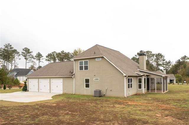 rear view of property featuring a garage, a lawn, concrete driveway, a chimney, and central air condition unit