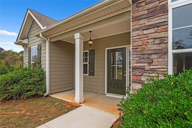 entrance to property featuring covered porch, stone siding, and a shingled roof